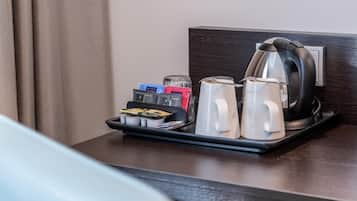 A hotel room with a dark wooden headboard, a tray with a kettle, two white mugs, and a set of toiletries.