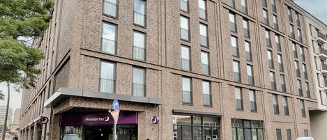 A multi-story brick building with a Premier Inn hotel entrance, a parking area, and a car parked in front.