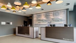 A hotel reception area with a modern design, featuring a large wall with inspirational words and phrases, two reception desks labeled 'Premier Inn,' and multiple pendant lights. - Premier Inn Hamburg City Klostertor (Hamburg)