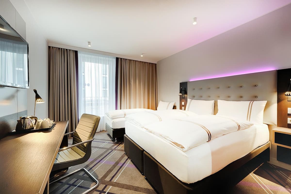 A hotel room with a large bed, a desk with a chair, a TV, and a bedside table.