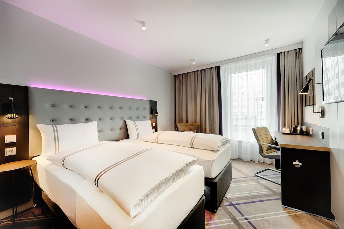 A hotel room with two beds, a desk, a chair, a wardrobe, and a large window with curtains.
