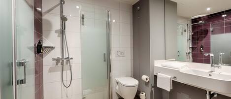 Un baño moderno con ducha de vidrio, inodoro blanco y tocador doble.