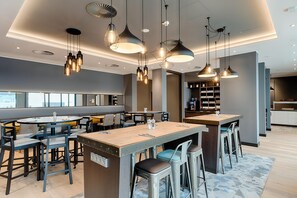 Zona de bar moderna con varias opciones de asientos, iluminación colgante y una barra visible.