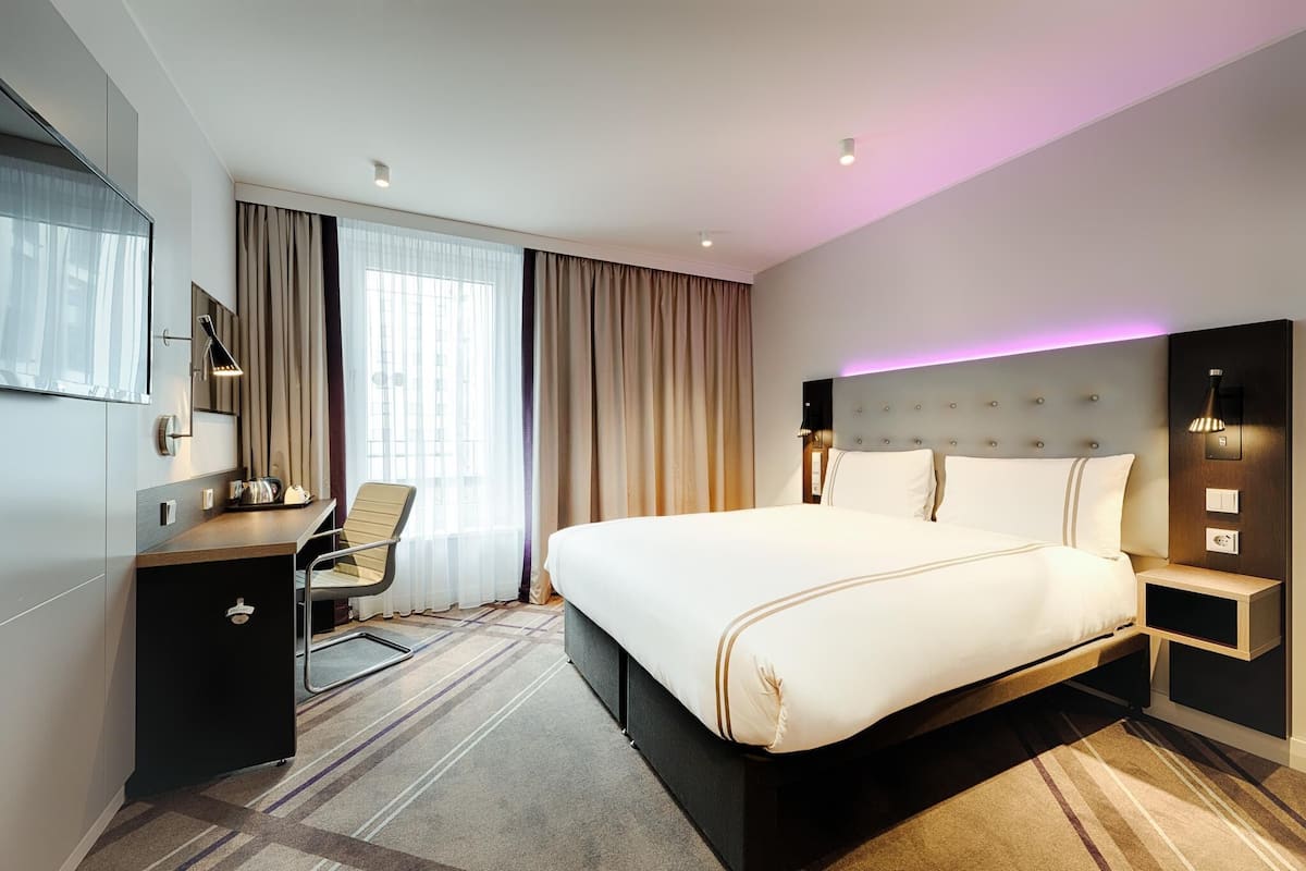 A modern hotel room with a large bed, a desk, a chair, and a TV.