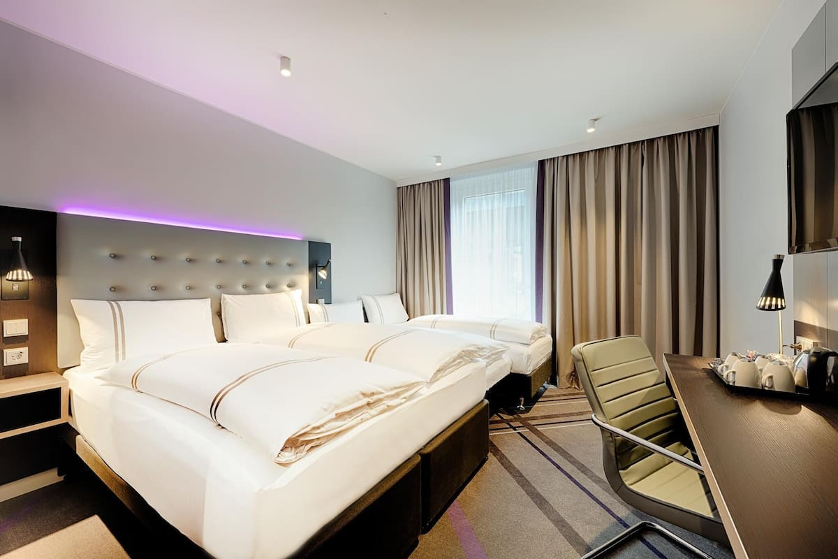 A hotel room with a large bed, a desk with a chair, a flat-screen TV, and a window with curtains.