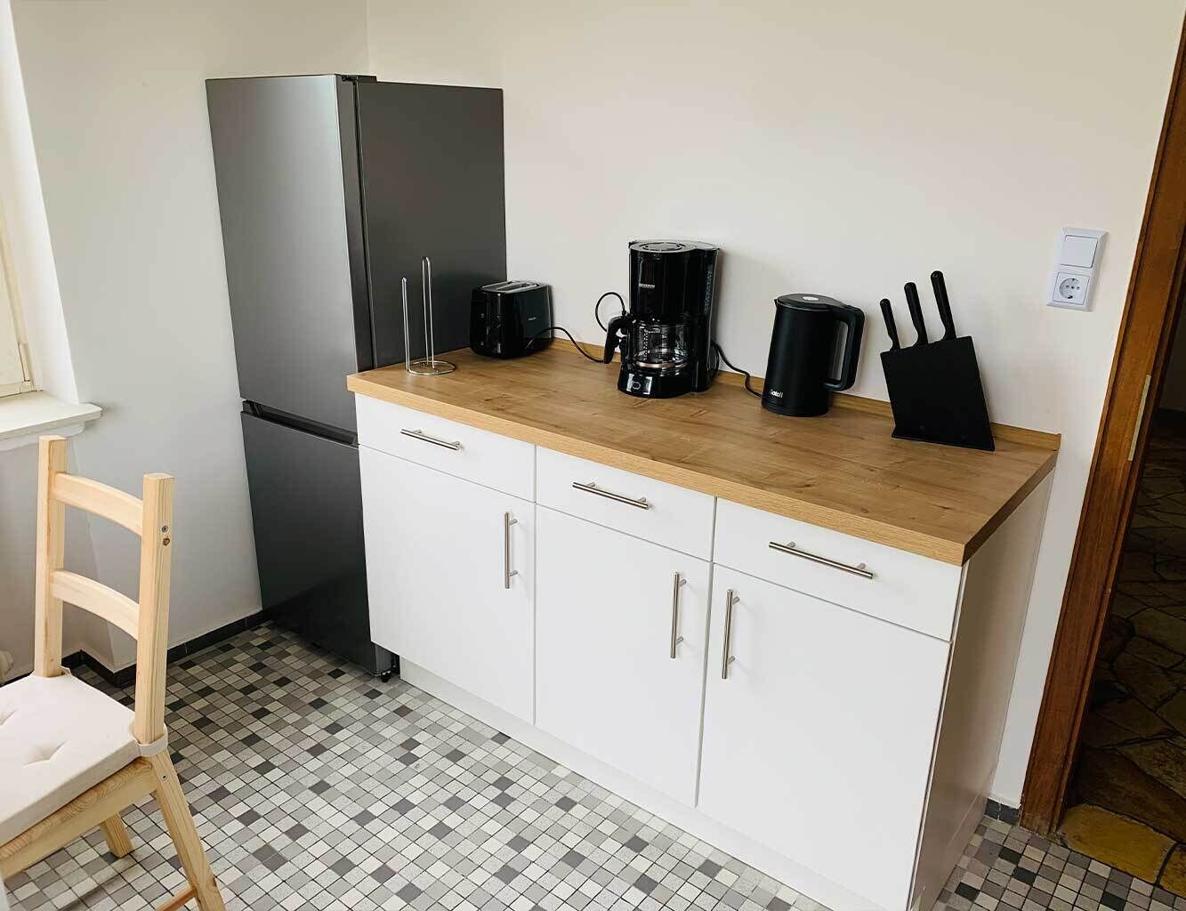 Eine kleine Küche mit Kühlschrank, Kaffeemaschine und einem Messerblock auf der Arbeitsplatte.