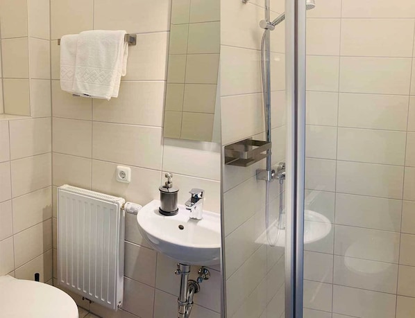 Un baño con lavamanos blanco, una toalla colgada en la pared, un espejo y una cabina de ducha de vidrio.