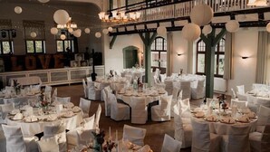 A banquet hall with round tables set for a formal event, white chairs, chandeliers, and a 'LOVE' sign in the background. - Fährhaus Kirschenland (Jork)