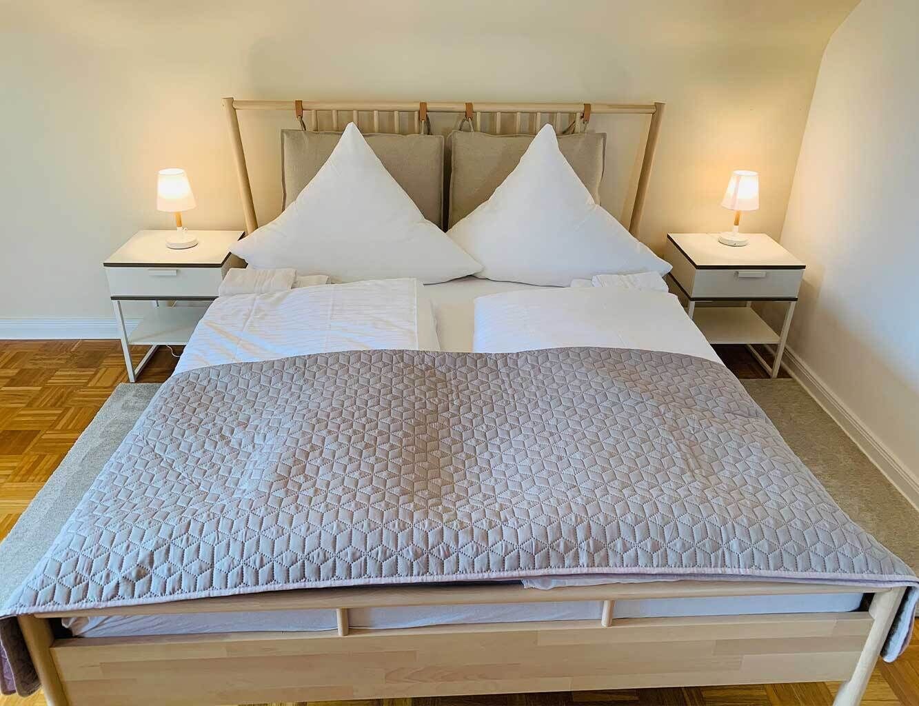 Una cama bien hecha con cubrecama acolchada, dos mesitas de noche con lámparas y un cabecero de madera.