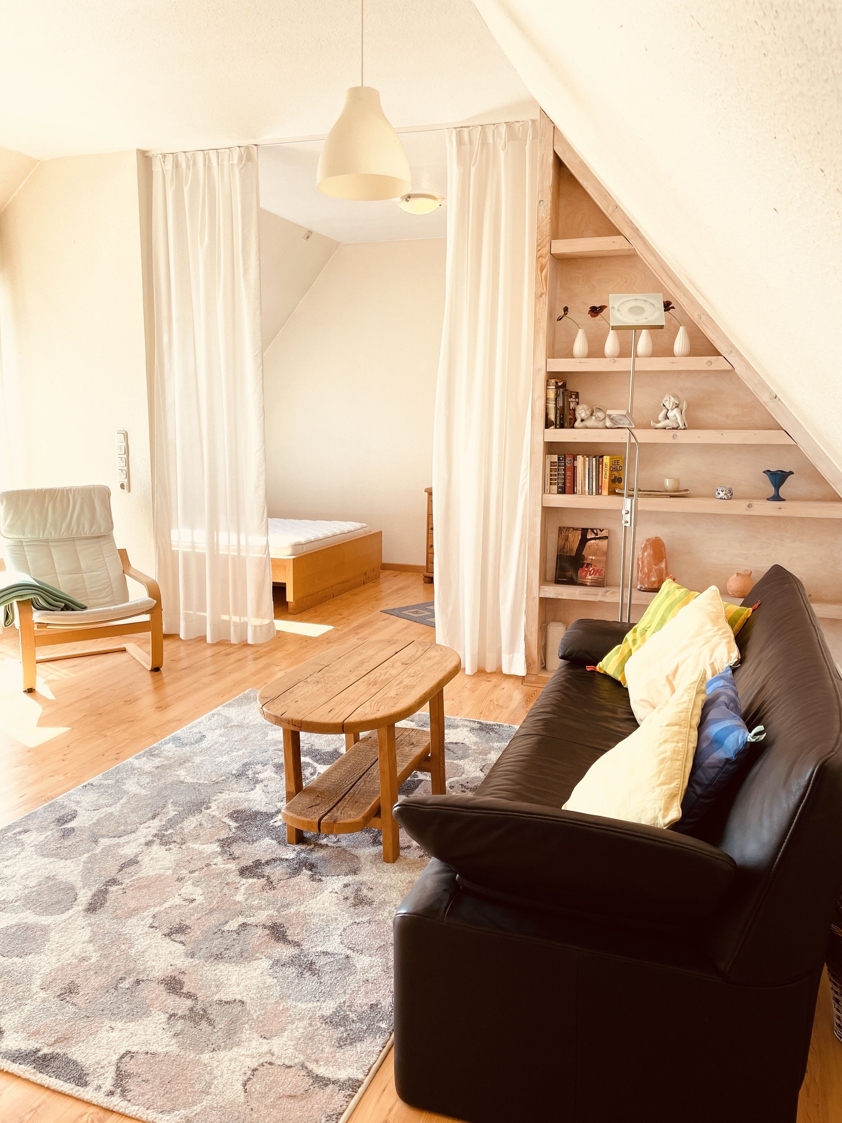 A cozy living room with a black sofa, a wooden coffee table, a chair, and a bookshelf.