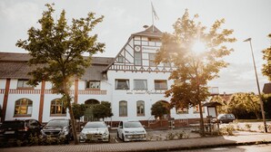 A traditional half-timbered building with a sign indicating it is a hotel. There are parked cars in front, and a flag is flying atop the building. - Fährhaus Kirschenland (Jork)