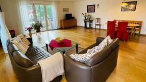 A living room with a sofa, coffee table, and a dining area with chairs and a table. - Fährhaus Kirschenland (Jork)