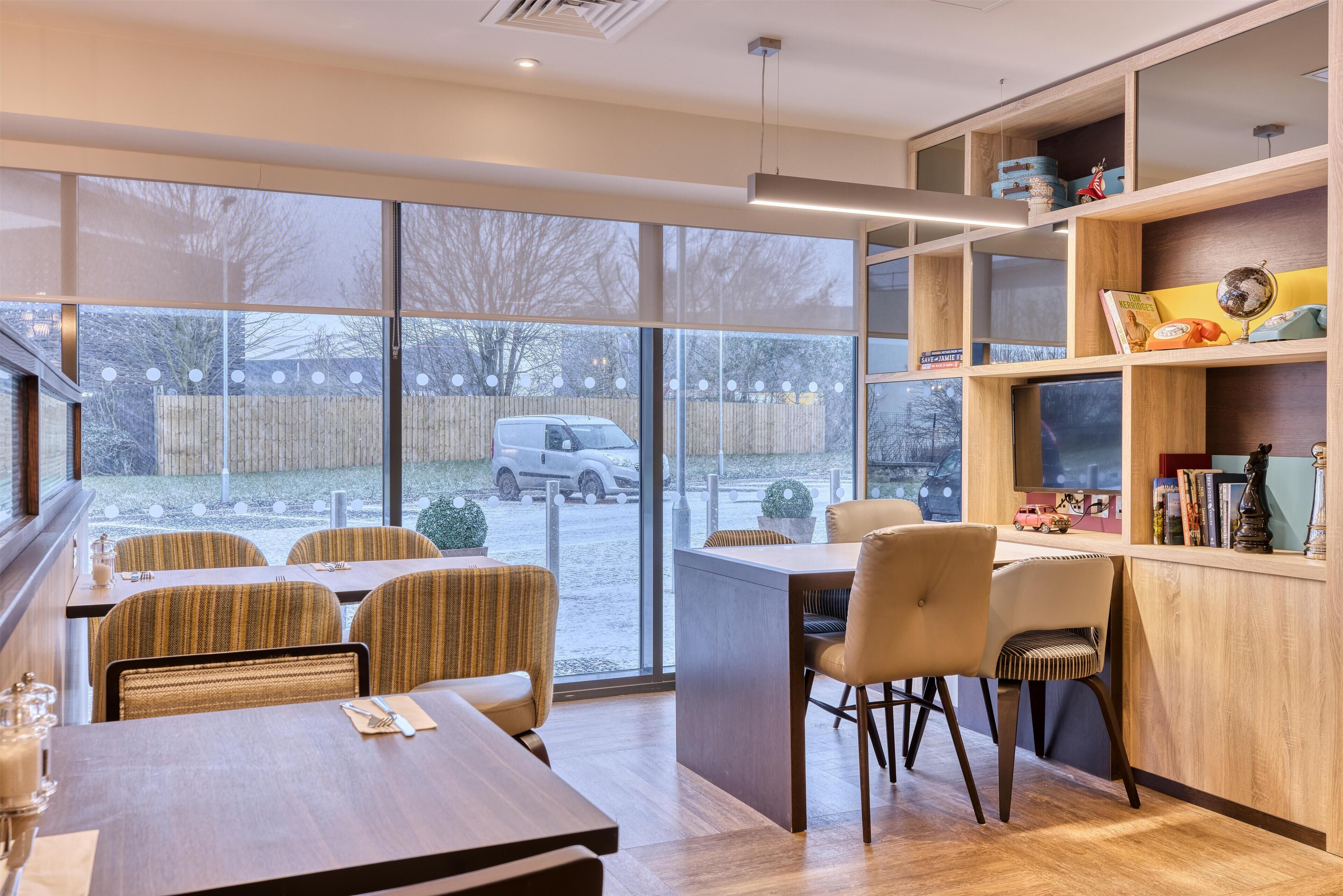 A modern dining area with a large window, wooden furniture, and a bookshelf.