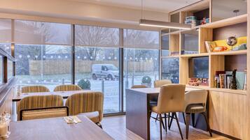 A modern dining area with a large window, wooden furniture, and a bookshelf.