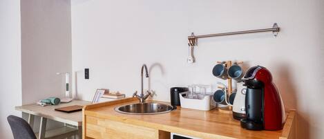 Una kitchenette compacta con un lavamanos, un microondas, una cafetera y un mueble pequeño.
