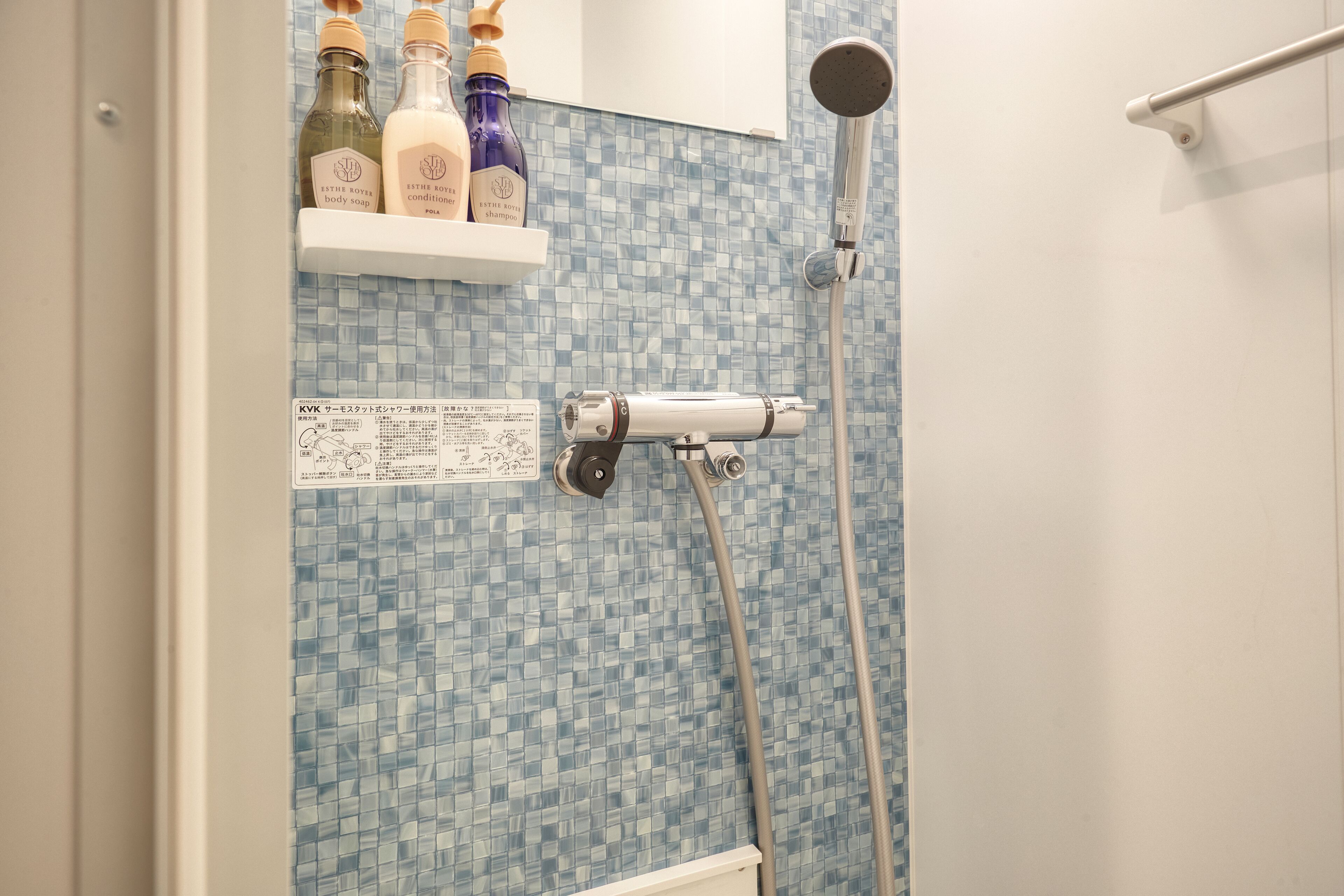 A bathroom with a shower, a white shelf with toiletries, and a tiled wall.
