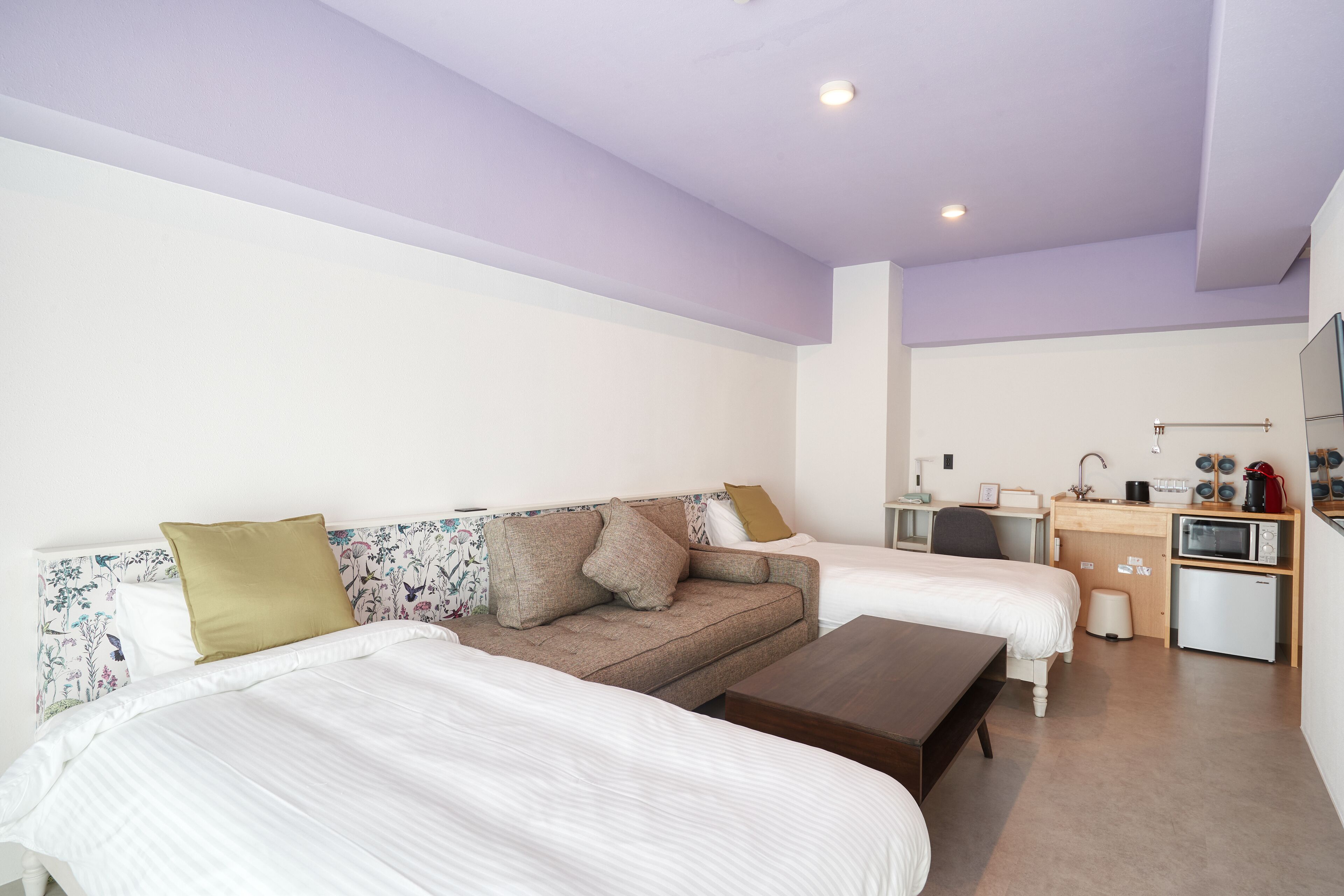 A bedroom with two beds, a sofa, a small desk, and a kitchenette.