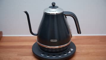 A DeLonghi electric kettle on a wooden table against a plain wall.