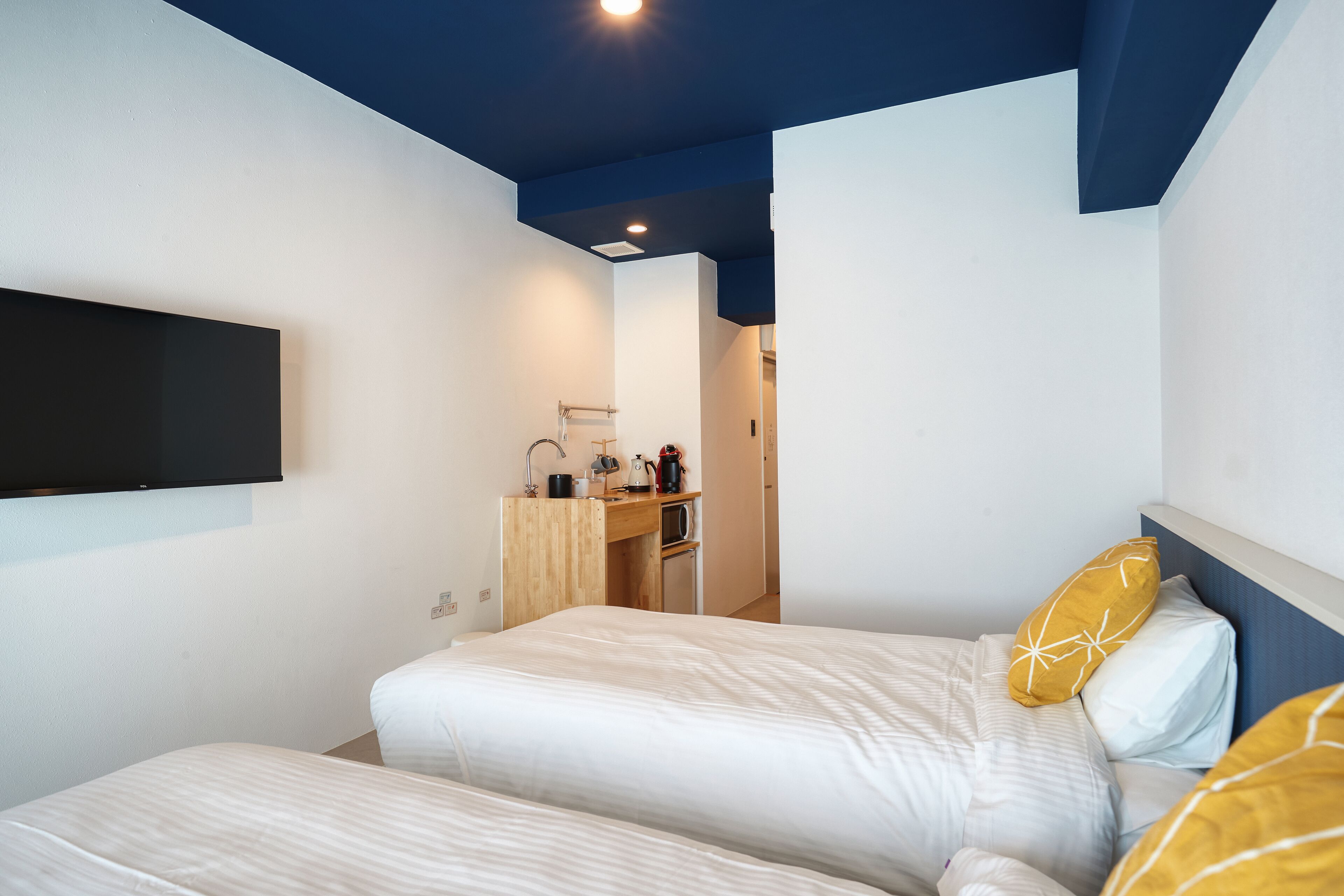 Una camera da letto con due letti, una scrivania e una TV a parete.