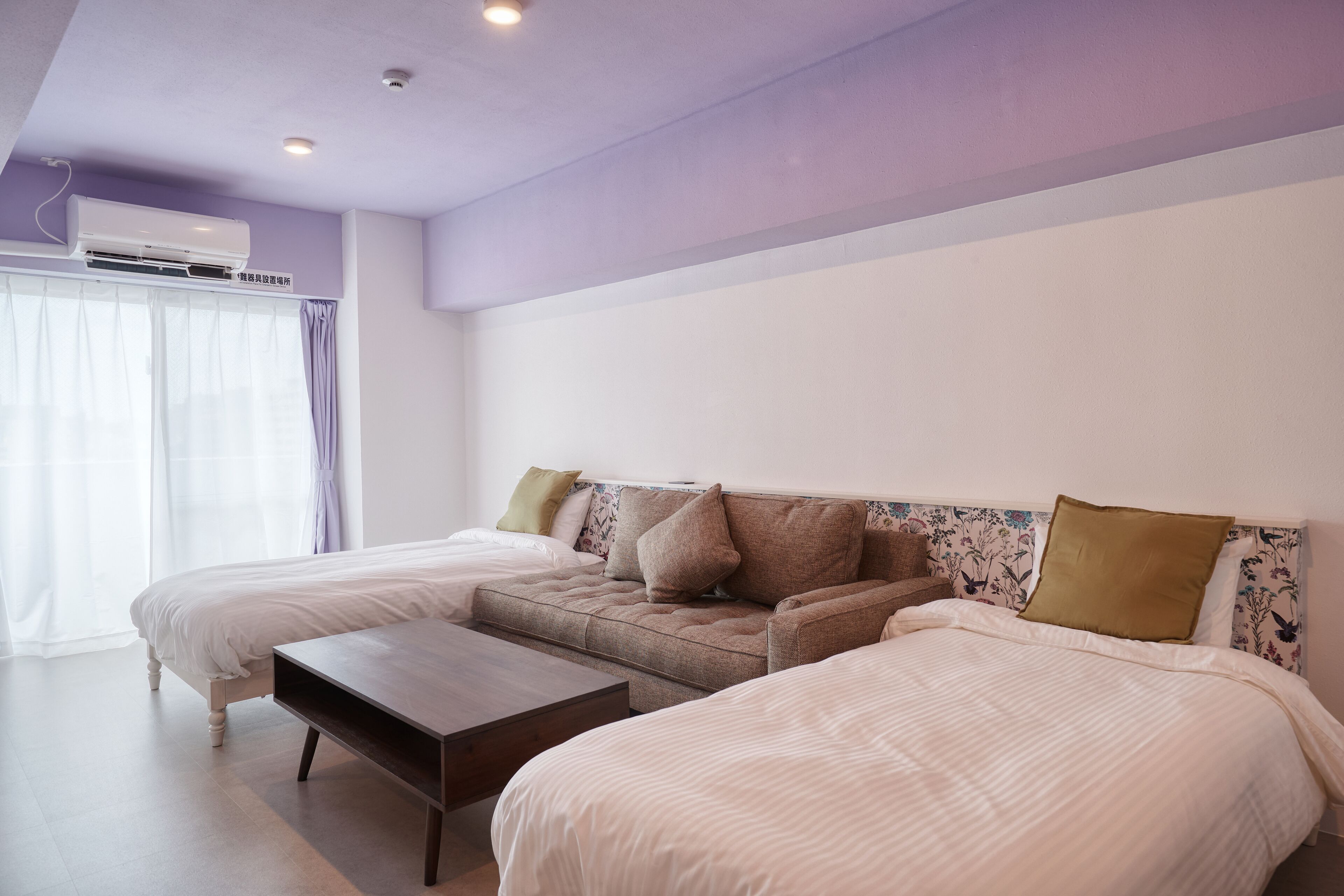 A bedroom with two beds, a sofa, a wooden coffee table, and an air conditioning unit.