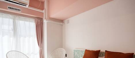 A hotel room with a bed, two chairs, a window with curtains, and an air conditioning unit.
