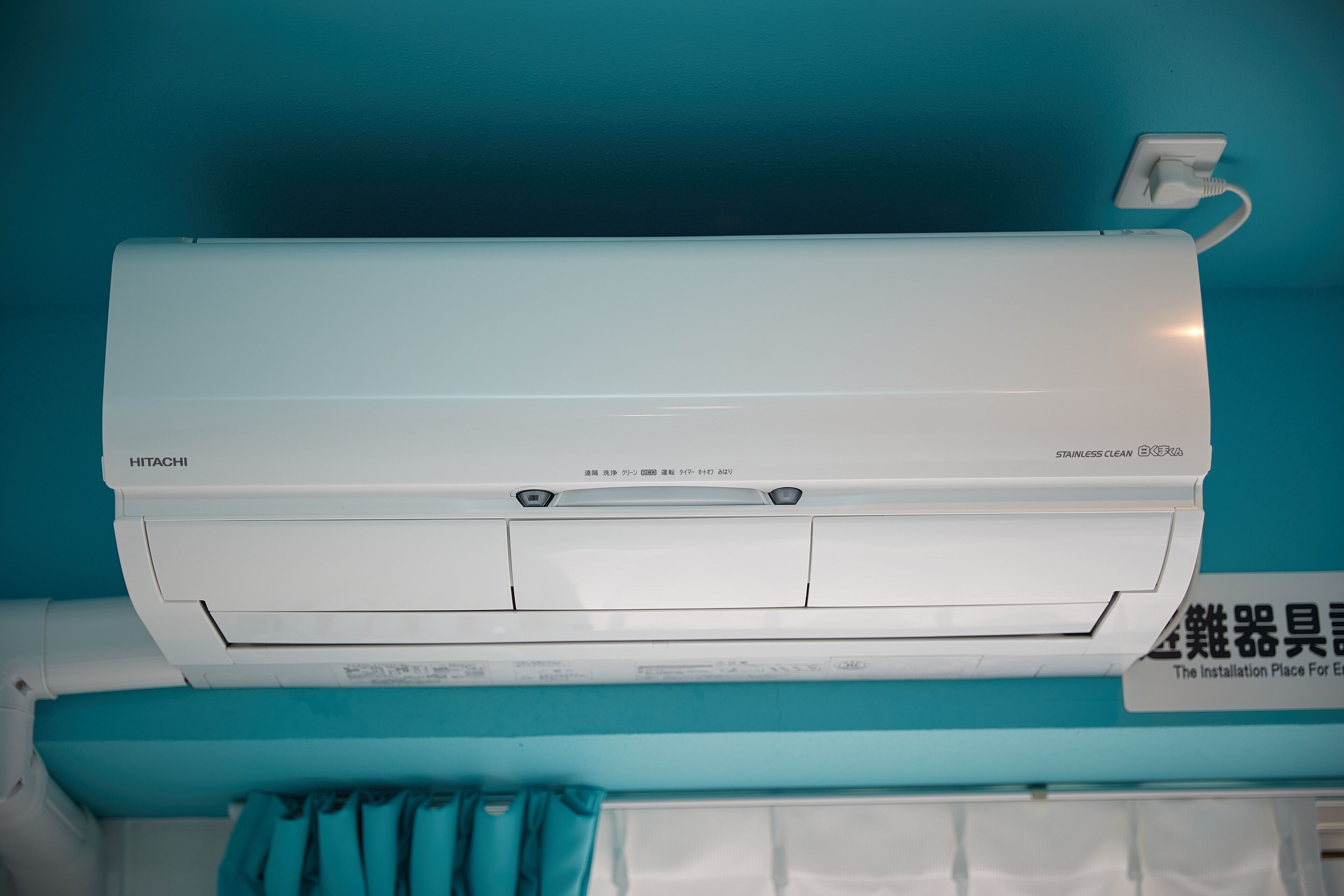 A HITACHI air conditioner mounted on a teal wall with a sign indicating it is the installation place for equipment.