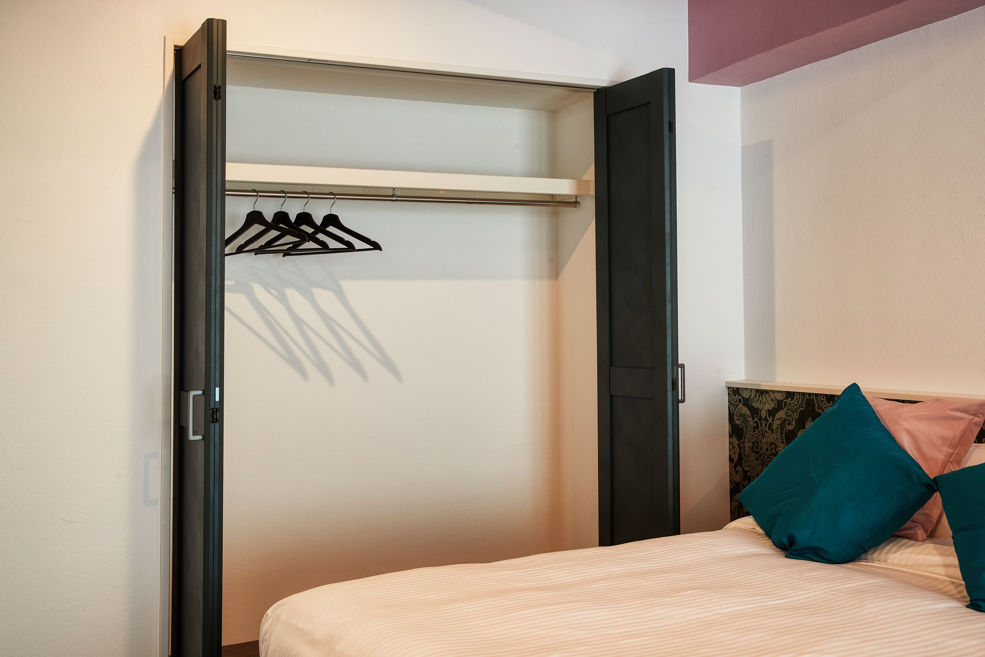 A bedroom with a bed, a closet with a hanging rod, and a headboard with decorative pillows.