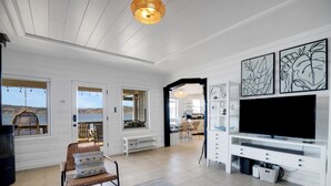 A spacious living room with a large TV, white walls, and a view of the outdoors.