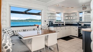 A modern kitchen with white cabinetry, a wooden dining table, and a view of the sea.