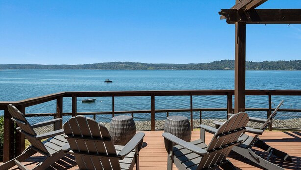 A wooden deck with Adirondack chairs overlooking a lake.
