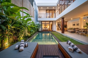 Relax in a serene outdoor space surrounded by lush tropical plants and enjoy a pool area with a wooden deck.