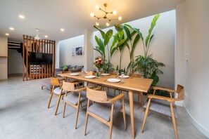A dining area with a wooden table and chairs, a TV mounted on a wooden partition, and large green plants. - 4BR Luxury Modern Contemporary Villa in Canggu (Canggu)