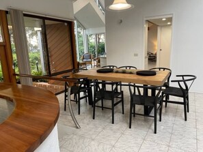 A dining area with a wooden table and black chairs, a sliding glass door leading to a garden, and a staircase with a wooden railing. - *Direct Access to Orion Beach* Jervis Bay Beachfront (Vincentia)