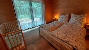 Une chambre dans une cabane en bois, avec un lit, une table de chevet, une lampe et un berceau.