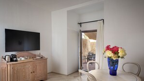 Una habitación con un armario de madera, un televisor de pantalla plana, una mesa de comedor con sillas y un florero con flores.