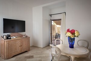 Una habitación con un armario de madera, un televisor de pantalla plana, una mesa de comedor con sillas y un florero con flores.
