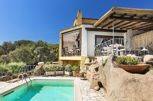 Zona de piscina con solárium de piedra, pérgola de madera y vistas a la montaña.
