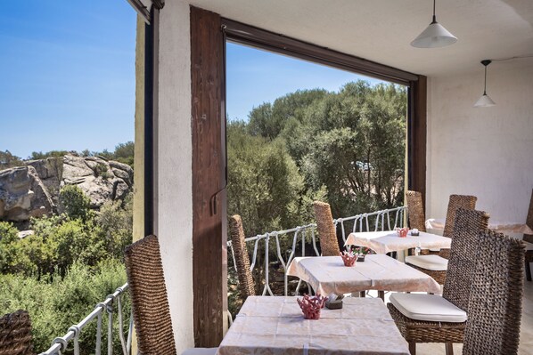 Un área de comedor al aire libre con muebles de mimbre y mesas, con vista a un paisaje rocoso y árboles.