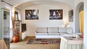 Una sala de estar con sofá, televisión, una mesa con lámpara y dos cuadros en la pared.