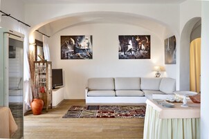 Una sala de estar con sofá, televisión, una mesa con lámpara y dos cuadros en la pared.