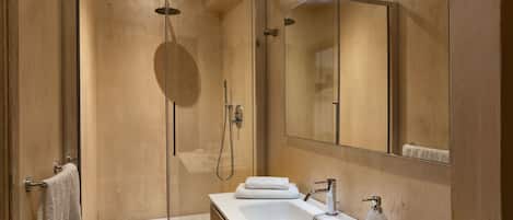 A modern bathroom with a glass-enclosed shower, a large mirror, and a white sink with a soap dispenser.