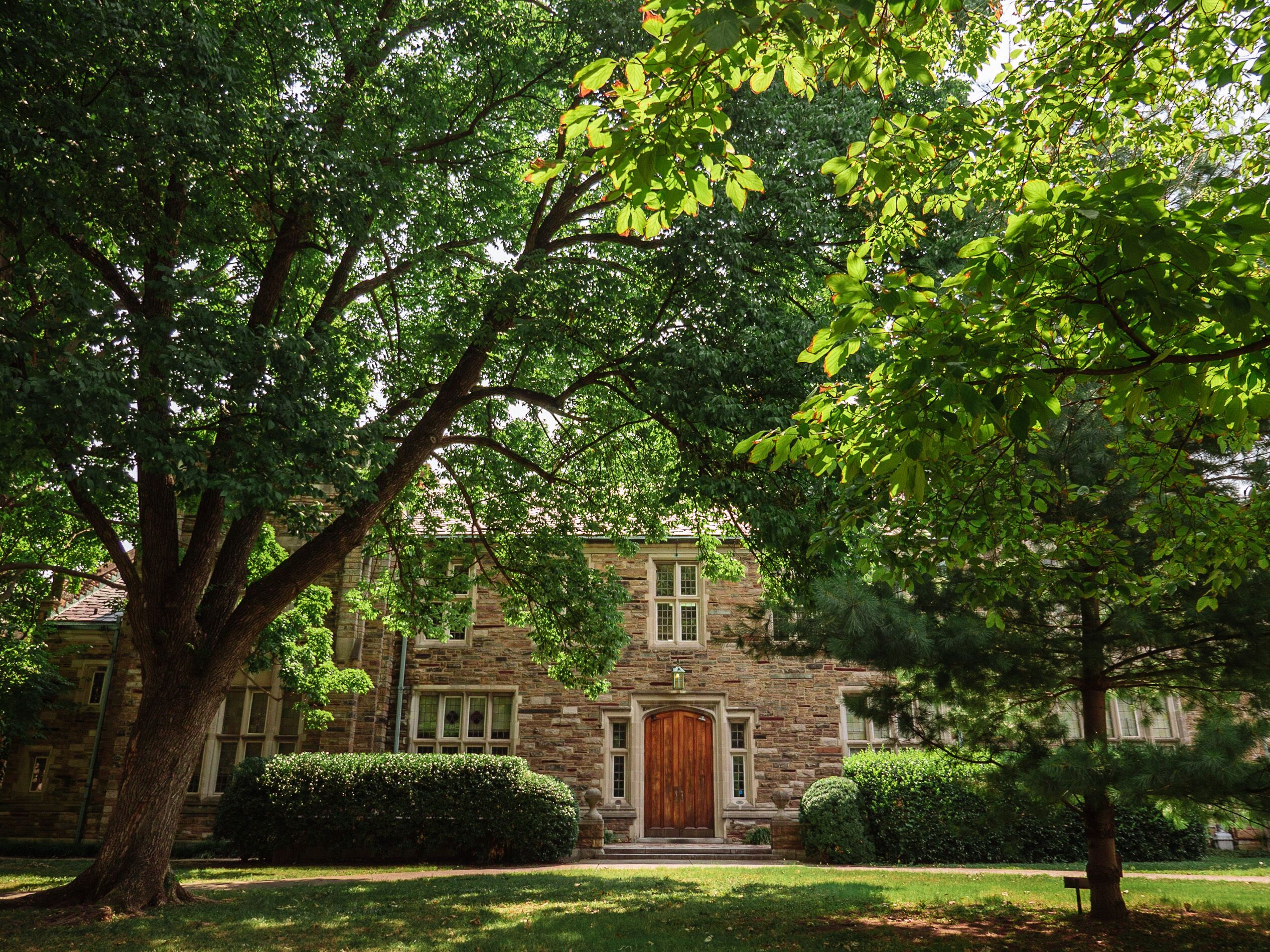 A stone building with a central entrance, surrounded by well-maintained lawns and trees.