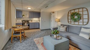 Un espacio habitable compacto con kitchenette, comedor y zona de estar con sofá y mesa de centro.