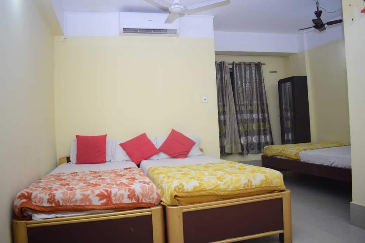 Une chambre avec deux lits, chacun agrémenté de draps à motifs floraux, un ventilateur de plafond et un appareil de climatisation.
