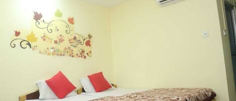 A bedroom with a bed, two red pillows, a floral bedspread, and a wall decoration with autumn leaves and flowers.