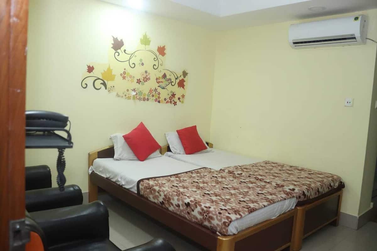 Une chambre à coucher avec un lit, deux oreillers rouges, une couvre-lit à motifs floraux, un bureau avec un téléphone et un appareil de climatisation fixé au mur.