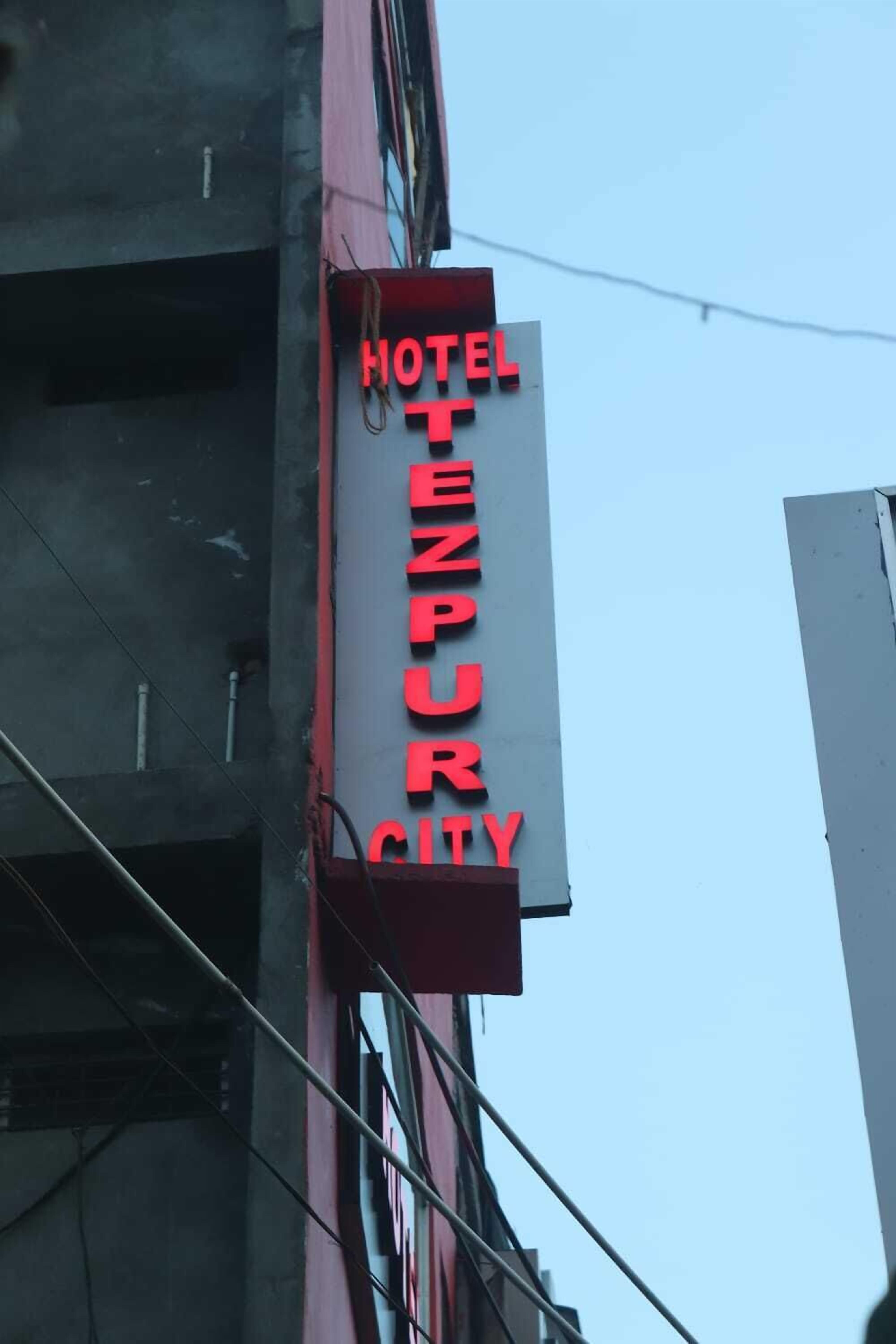 Une enseigne d’hôtel avec l’inscription « HOTEL TEZPUR CITY » en lettres rouges sur un fond blanc.