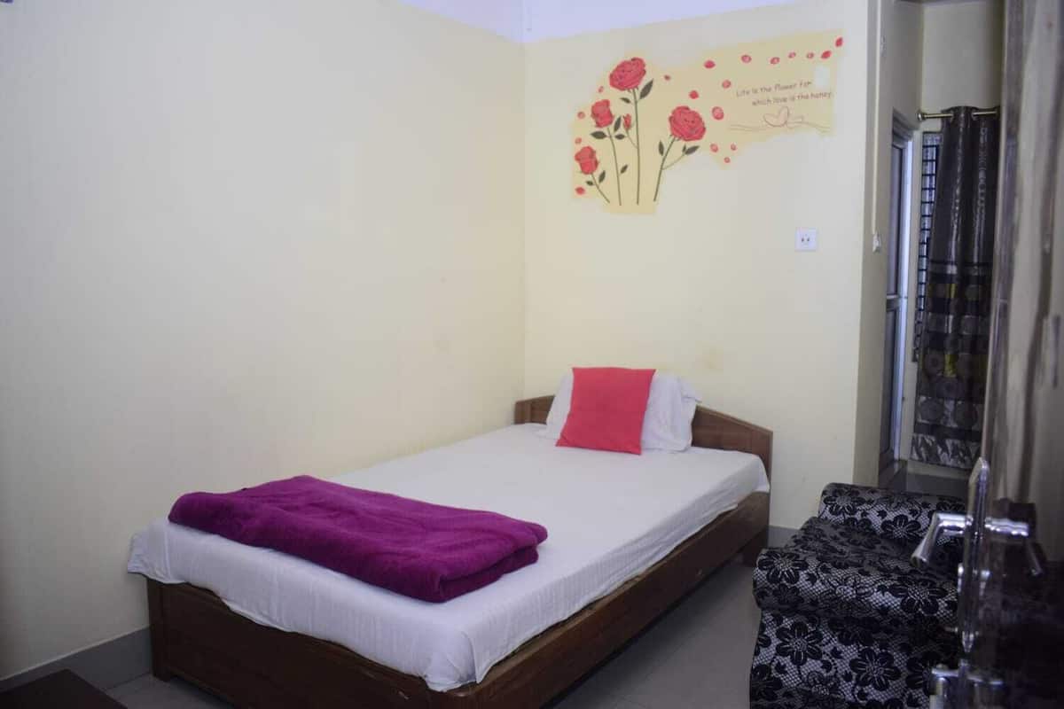 Une chambre avec un lit simple, un cadre en bois, du linge de lit blanc, un plaid violet, un coussin rouge et une décoration murale représentant des roses avec une citation.