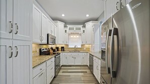 A modern kitchen with white cabinets, stainless steel appliances, and a patterned floor. - Flirty Flamingo- Pet-Friendly Vacation Home Near Beach with Private Pool Area (Destin)