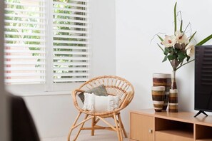 Relax in comfort with a wicker chair by the window, a flat-screen TV, and a vase with fresh flowers.